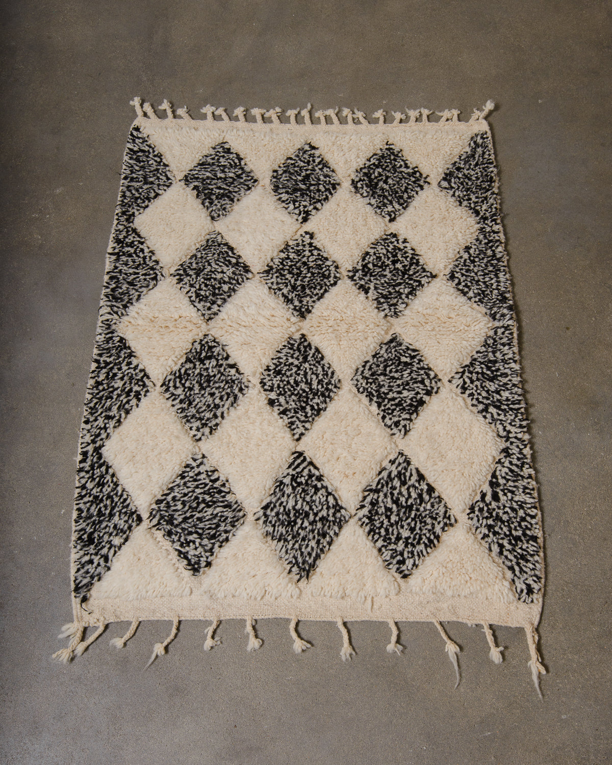 Small Berberlin Beniourain rug made of wool in black and white, laying on a concrete floor.
